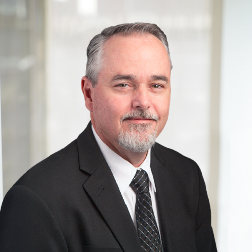 Corporate headshot of Mark Jones in color, wearing a dark suit jacket, white shirt and tie.