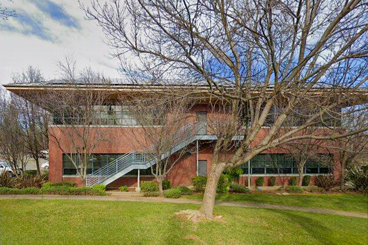 Exterior view of a brick office building with a large tree and green grass