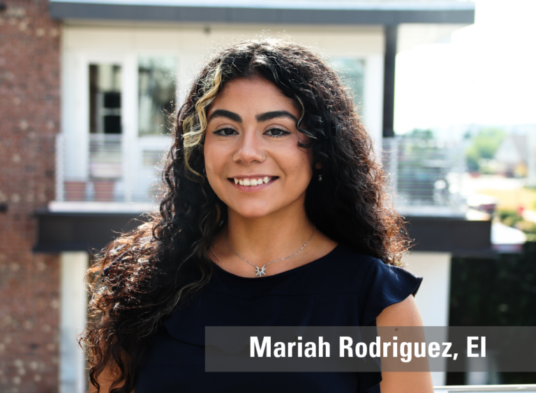 A professional outdoor headshot of a young smiling woman with curly hair wearing a black top