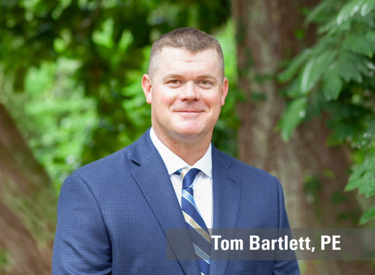 A professional outdoor headshot of a smiling man wearing a blue suit