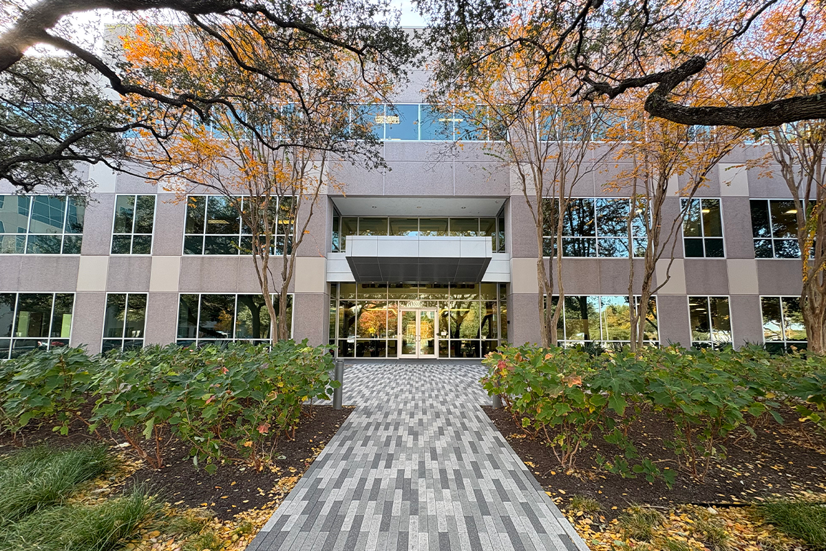 A large office building with glass doors, with trees and greenery in front