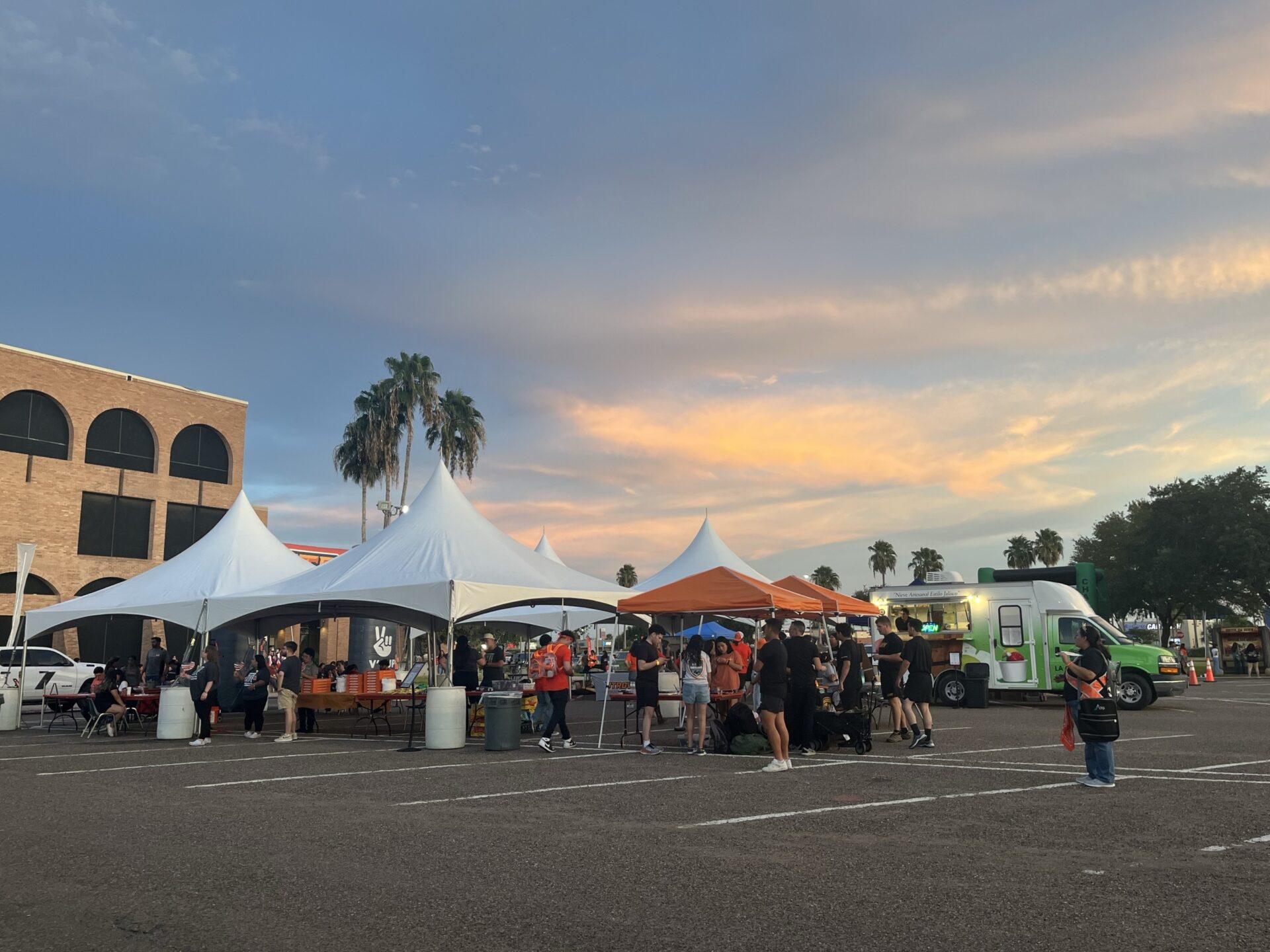 AN event in a parking lot at sunset with tents set up and a food truck