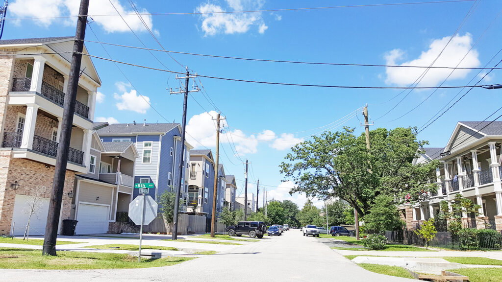 Residential street with overhead utility lines, utility poles, sidewalks, and homes.