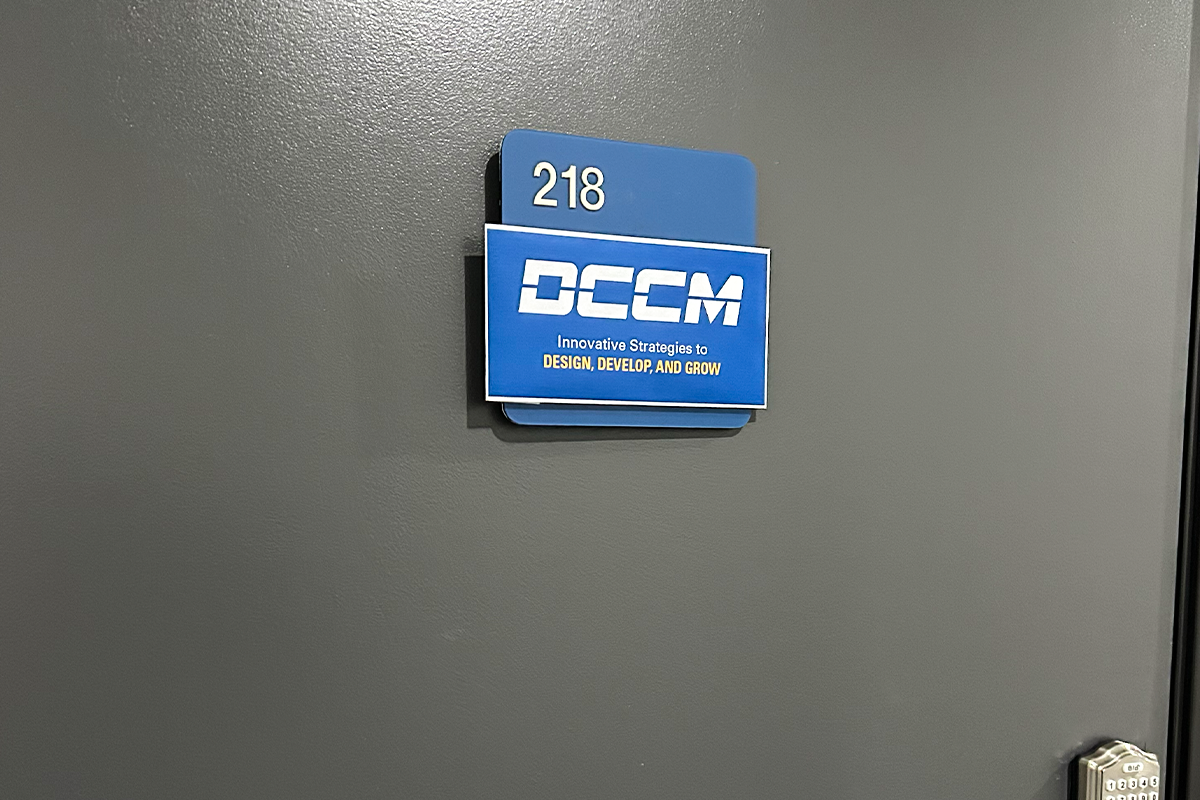 Blue signage on a grey office door with the DCCM logo and tagline